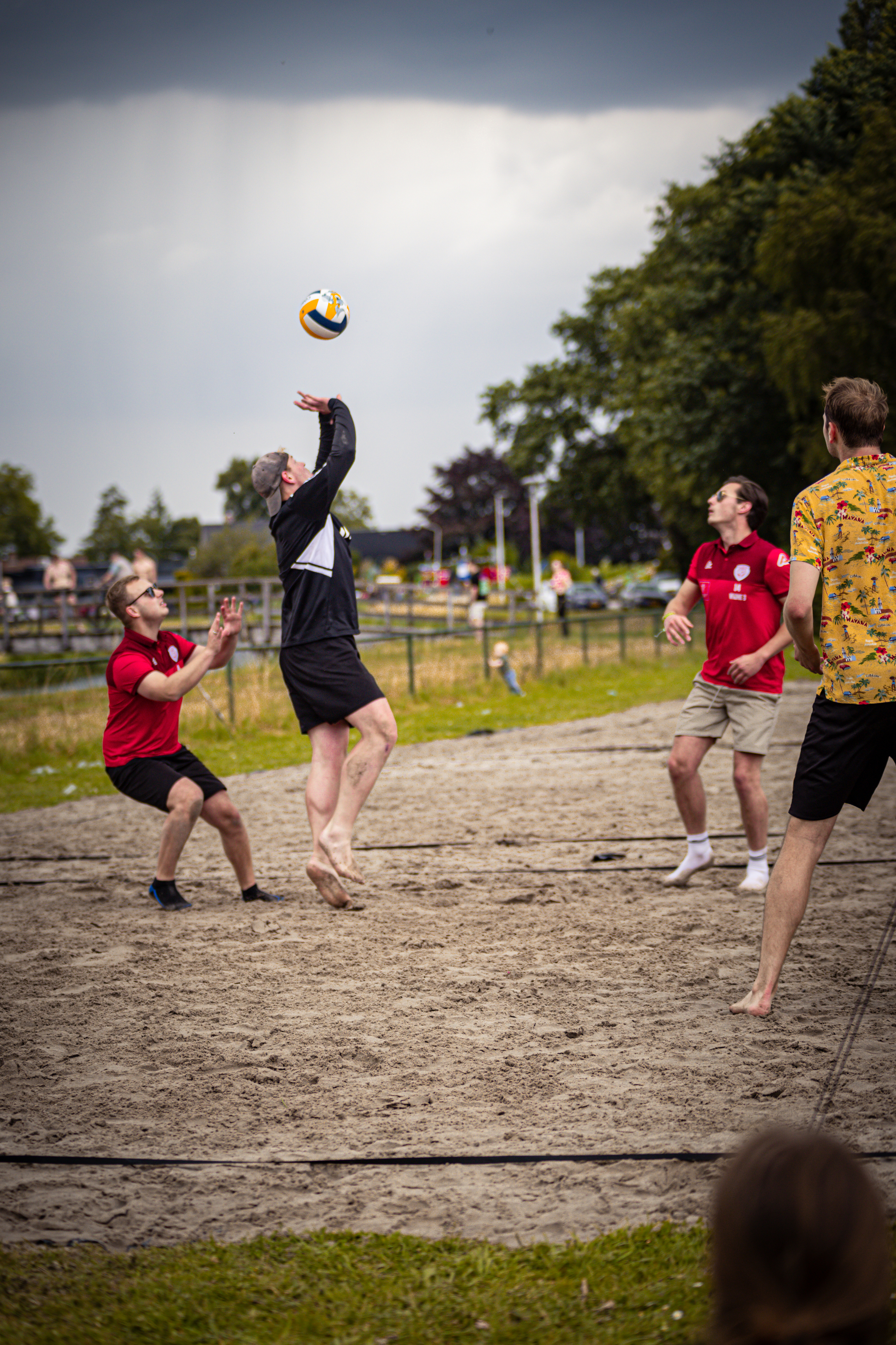 A man wearing a red shirt is about to hit a beach volleyball.