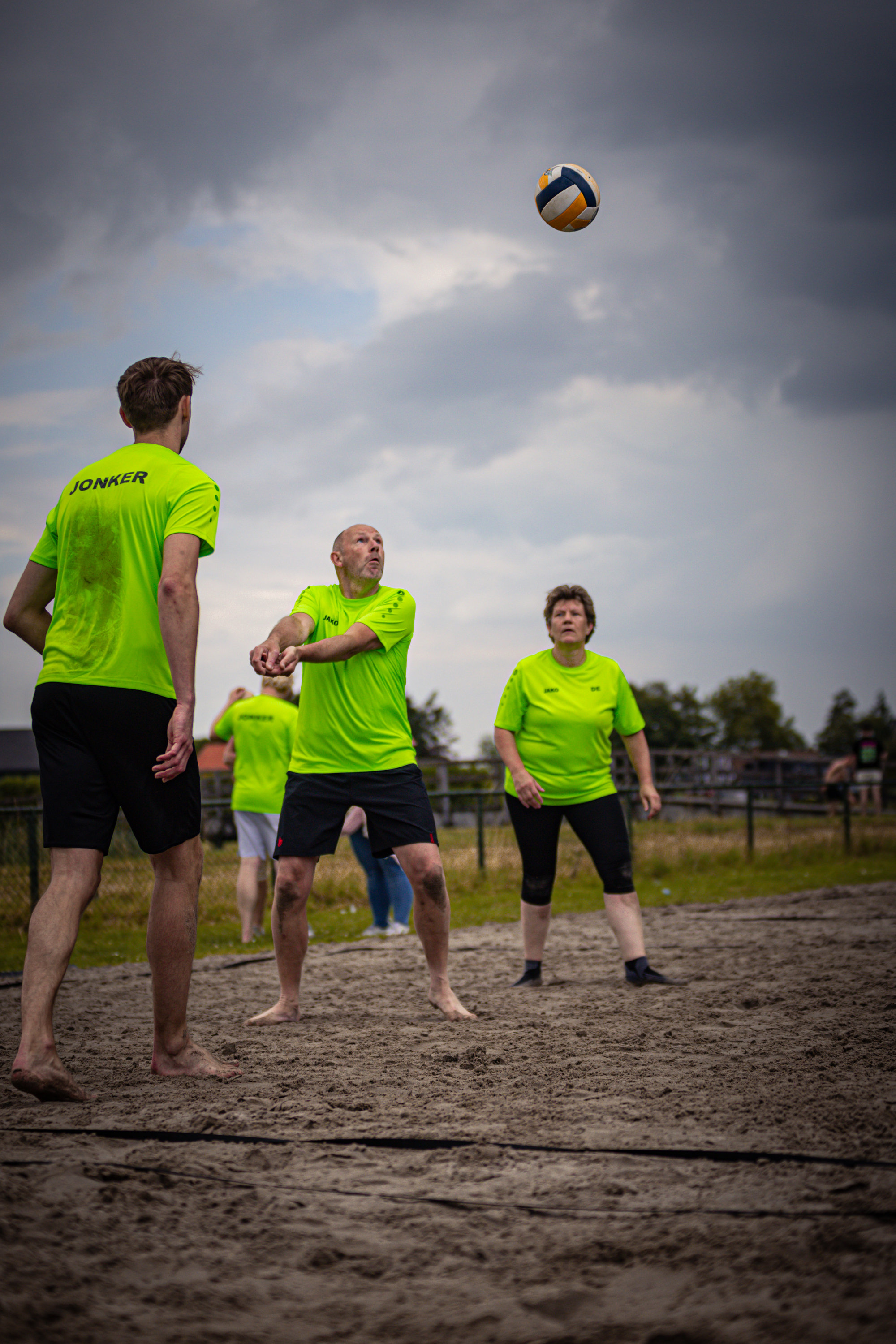 A group of men and women playing beach volleyball, wearing green shirts that say "Boerhaar".