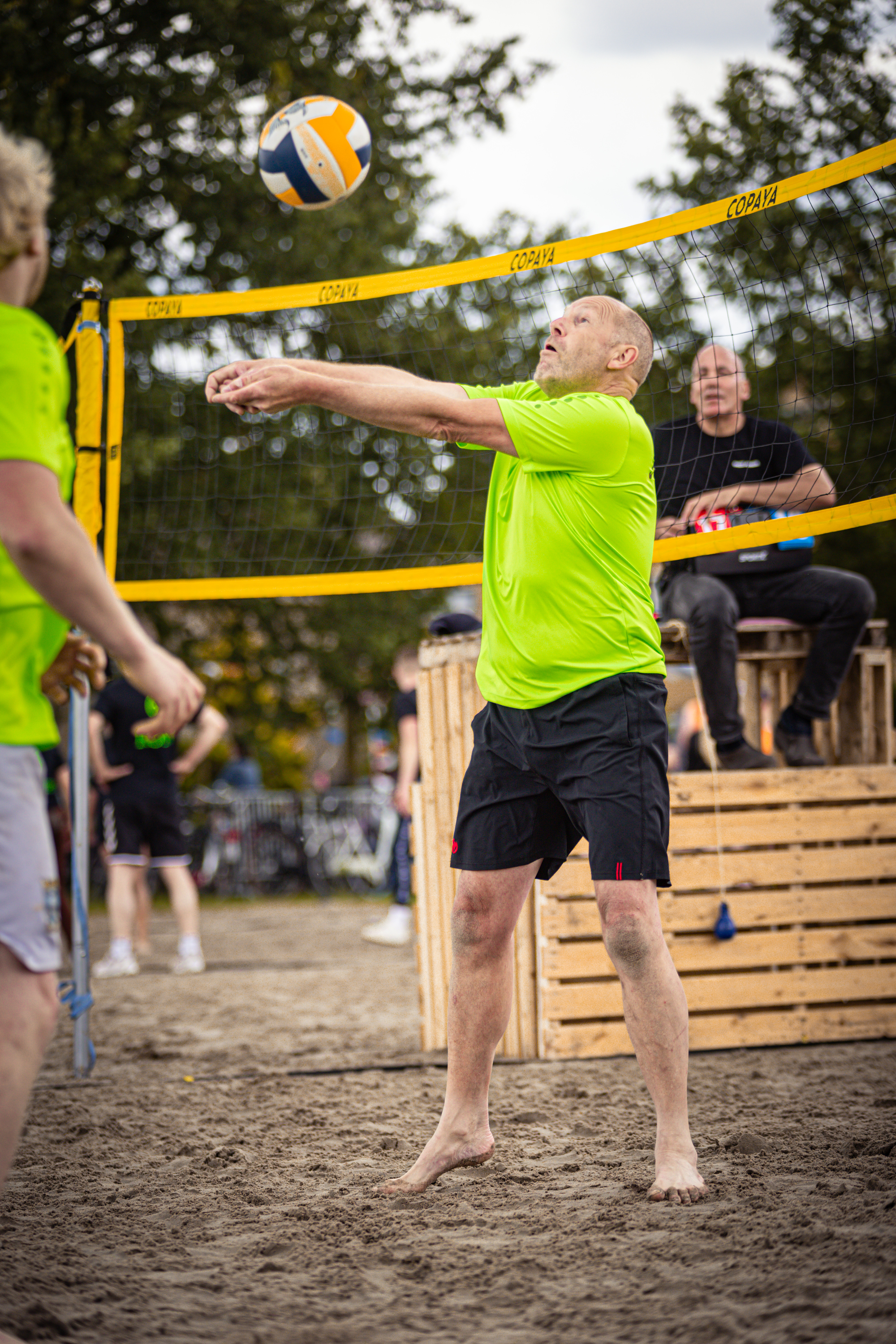 A man in a yellow shirt is playing beach volleyball.