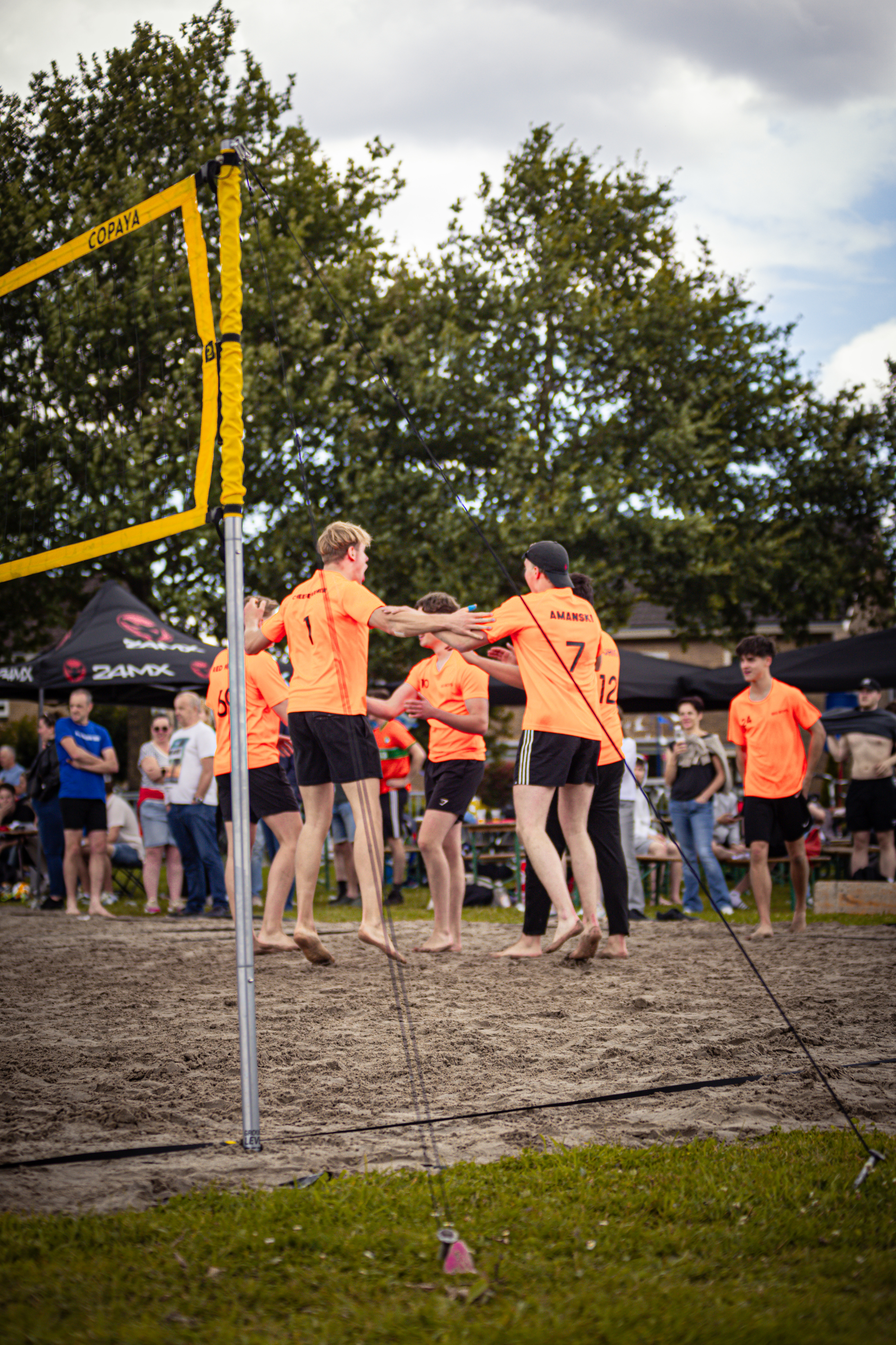 Volleyball players wearing orange shirts on a sandy field.