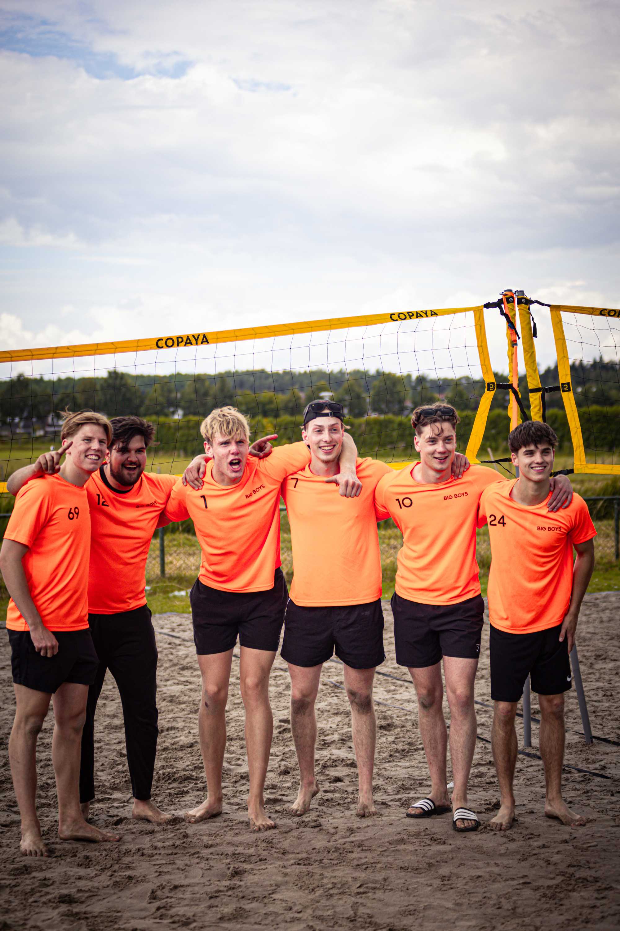 A group of guys are posing for a picture in front of a volleyball net.