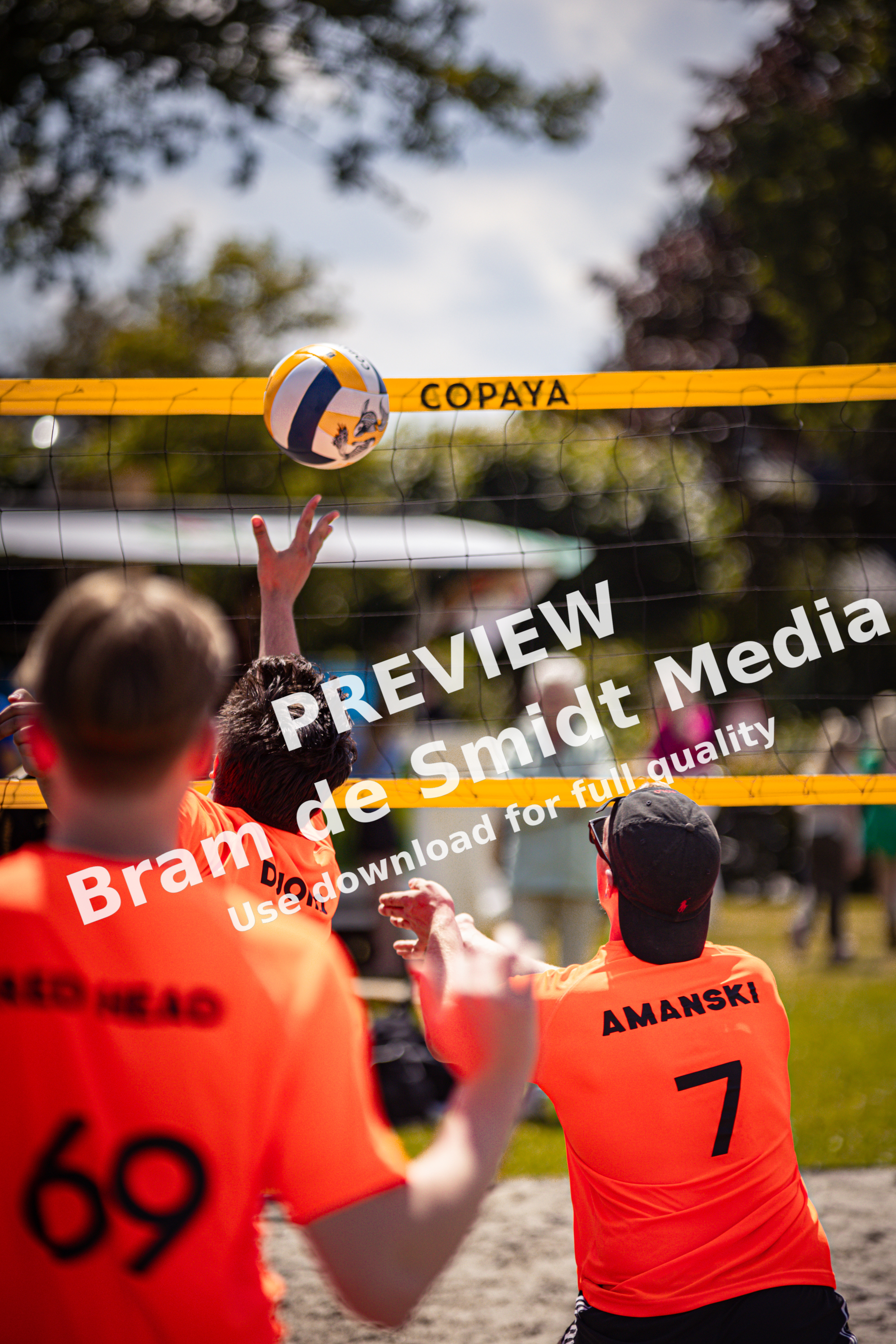 A group of people play beach volleyball, wearing orange shirts and shorts.