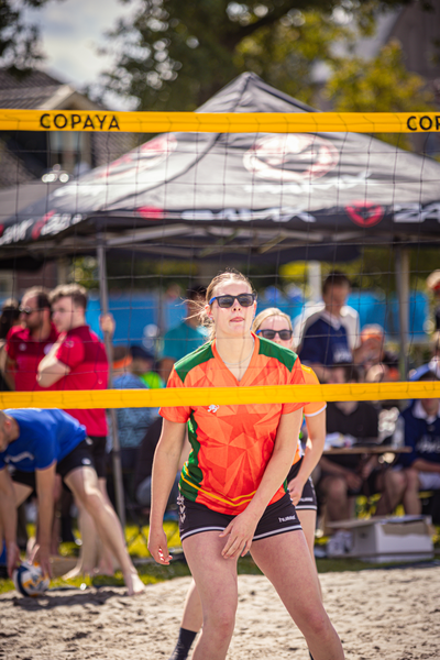 Two women play volleyball on the beach with people watching.