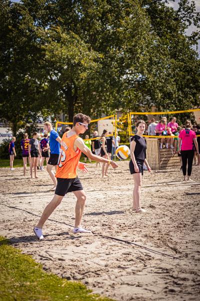 A group of people on a sandy beach are enjoying a game of volleyball.