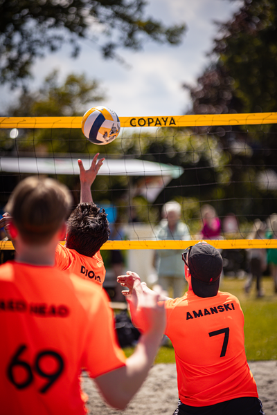 A group of people play beach volleyball, wearing orange shirts and shorts.