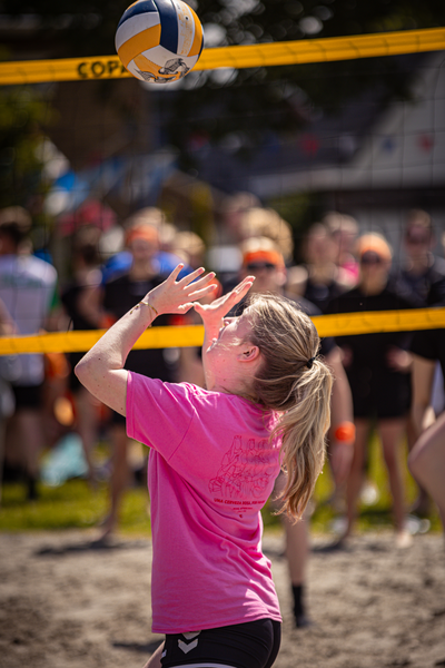 A girl in a pink shirt about to hit the volleyball with her head.