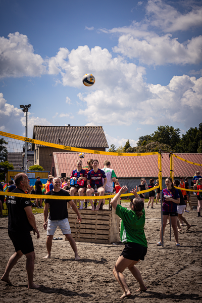 Volleyball players on a beach with a group of people watching and enjoying the game.