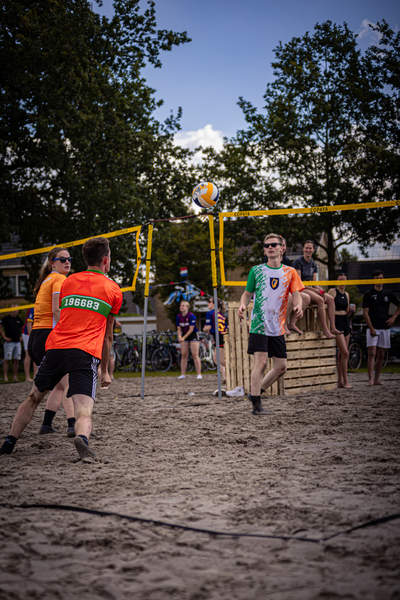 A group of people playing beach volleyball with one person holding a ball.