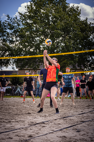 A group of people playing beach volleyball, one of the players is wearing an orange shirt.