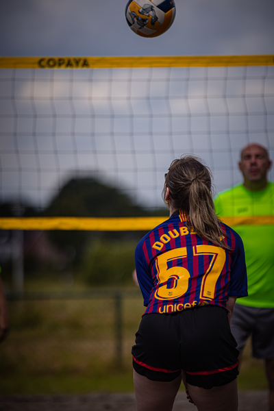 A girl with the number 57 on her jersey getting ready to hit a volleyball with a man in yellow behind her.