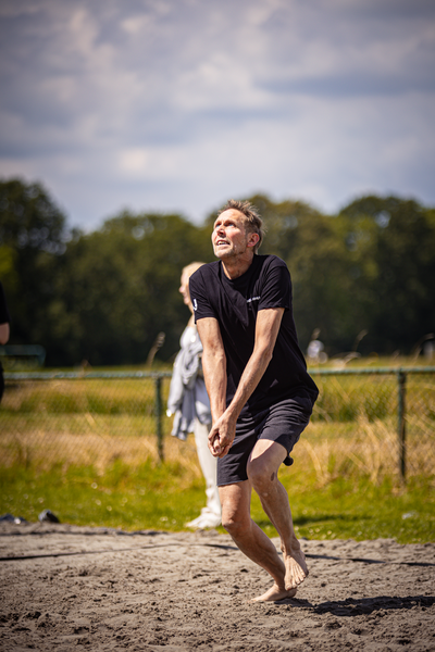 A man with a black shirt playing beach volleyball.