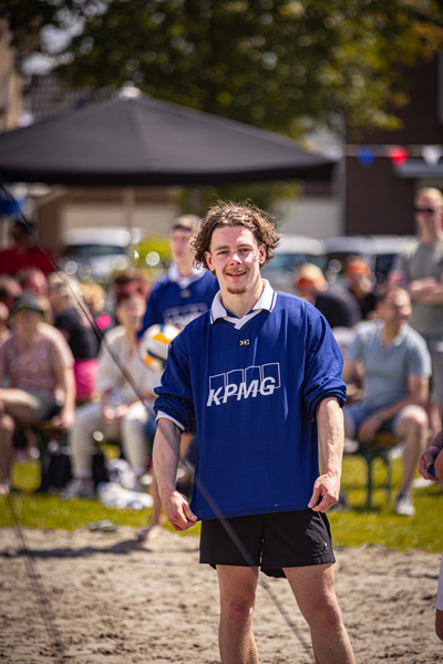 A boy in a blue shirt with the letter K on it stands on a sandy ground.