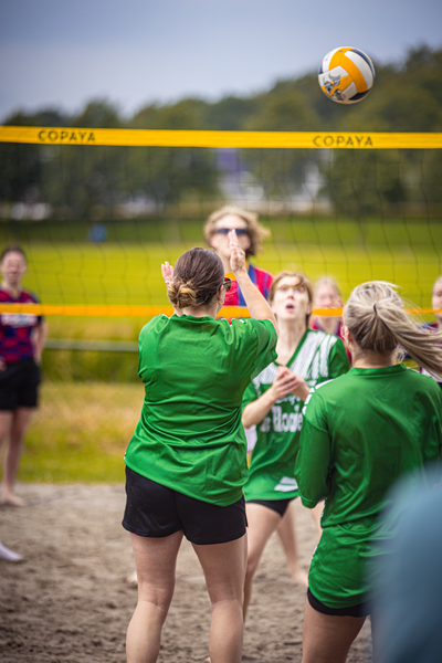 "Women's beach volleyball game with the name Kopaya on it and another woman looking up at a ball being hit.