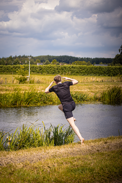 A person playing volleyball by a body of water in front of an orange and yellow sky.