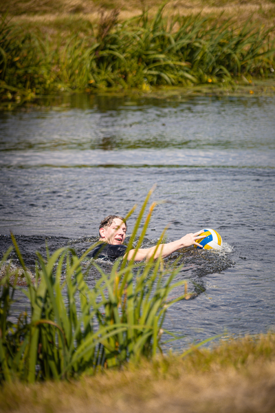 A boy playing beach volleyball in the water with a red ball.