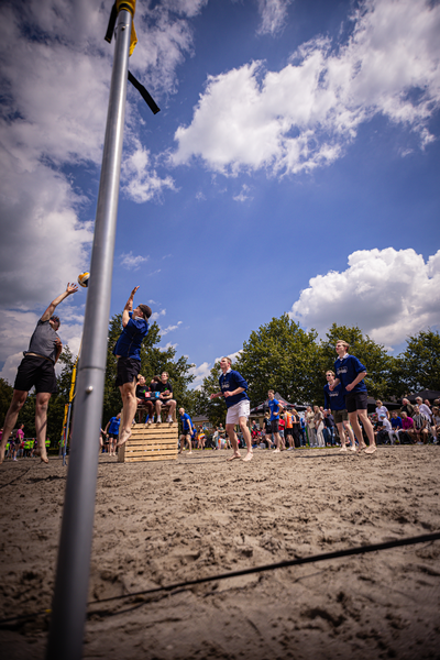 A man in a blue shirt prepares to hit a volleyball on the beach.