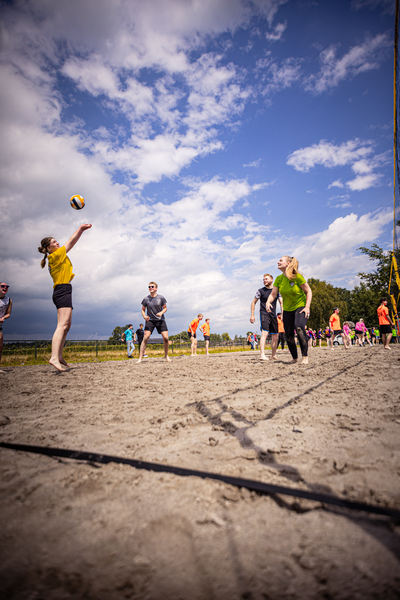 A woman is serving a volleyball in front of a group of other people, some wearing orange jerseys.