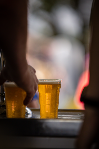 A person is holding two full beer glasses at a bar.