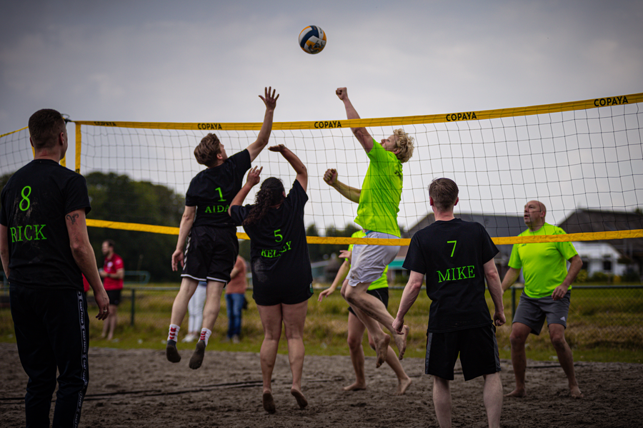 A group of people playing beach volleyball wearing black and yellow t-shirts.