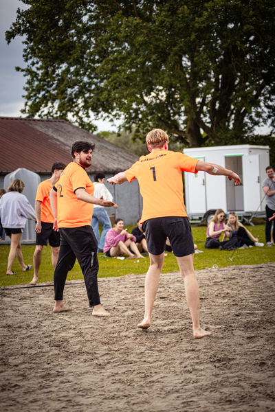 Two men are playing beach volleyball in orange shirts.