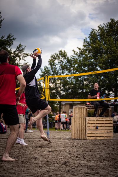 A group of people play beach volleyball, one of whom is wearing a red shirt.