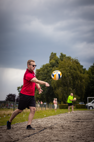 A man wearing sunglasses and a red shirt is playing beach volleyball with a ball on the court.