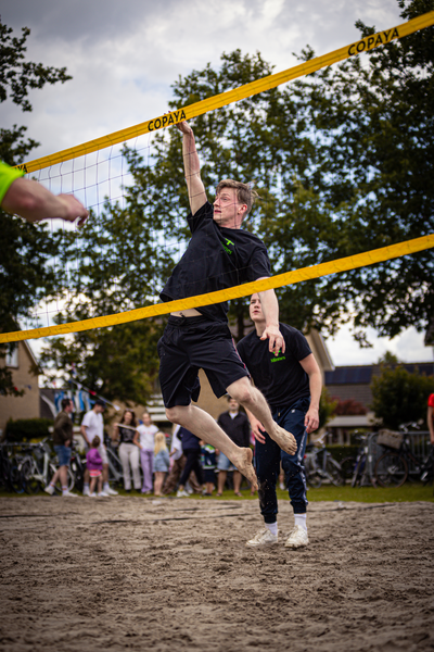 Two men playing beach volleyball, with one jumping in the air to hit the ball.