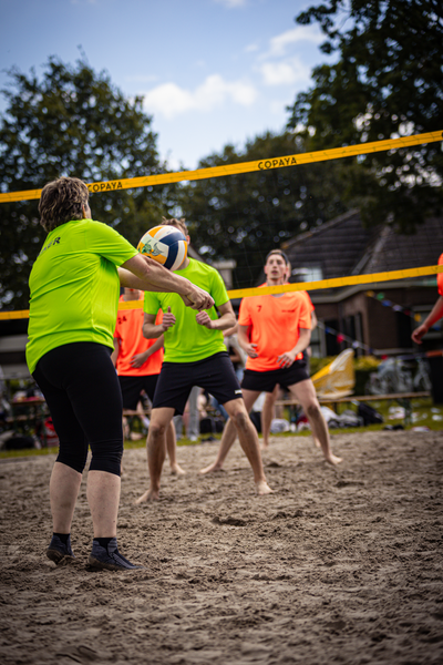 A group of men play beach volleyball in orange and green shirts.