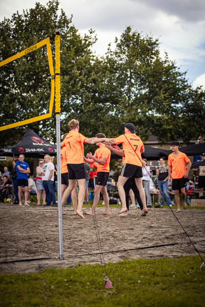 A group of people play beach volleyball, some wearing numbers like 7 and 16.