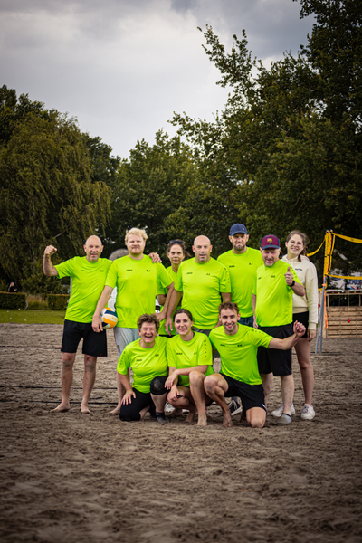 A group of 8 people posing for a picture with a volleyball in the background.