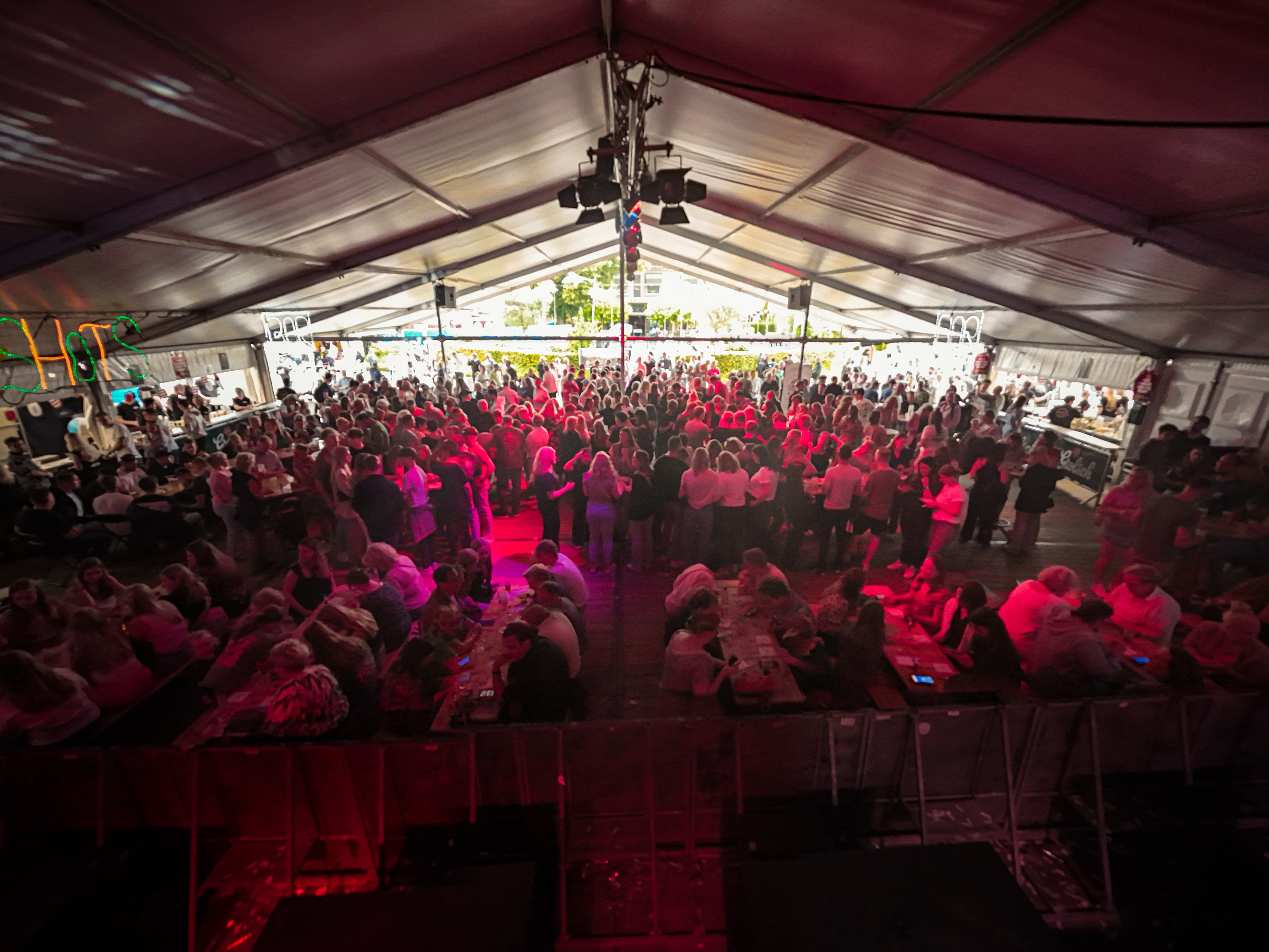 A large crowd of people at a festival with lots of lights and pink walls.