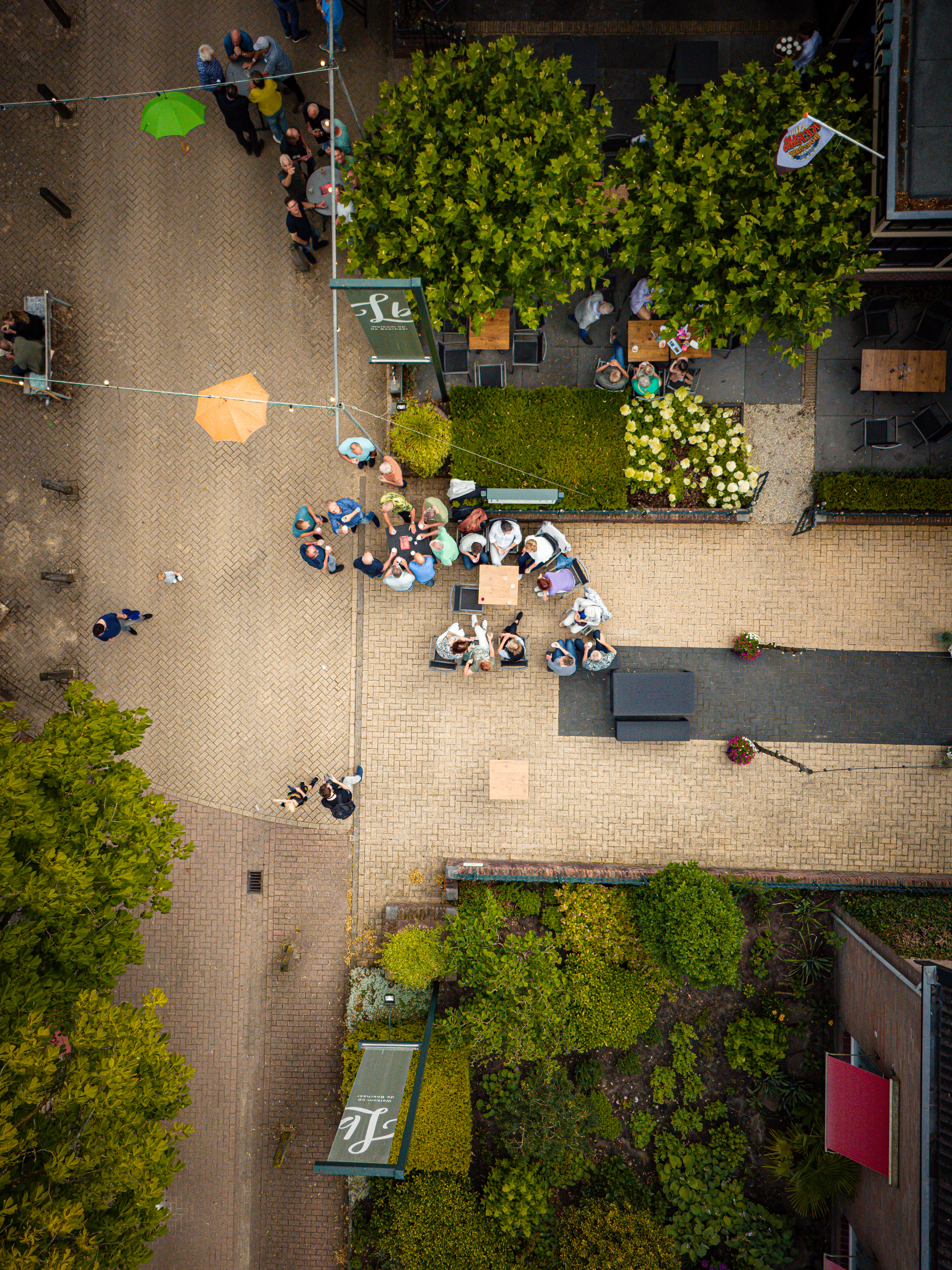 Several people are gathered in a courtyard with tables and umbrellas, enjoying an outdoor meal.