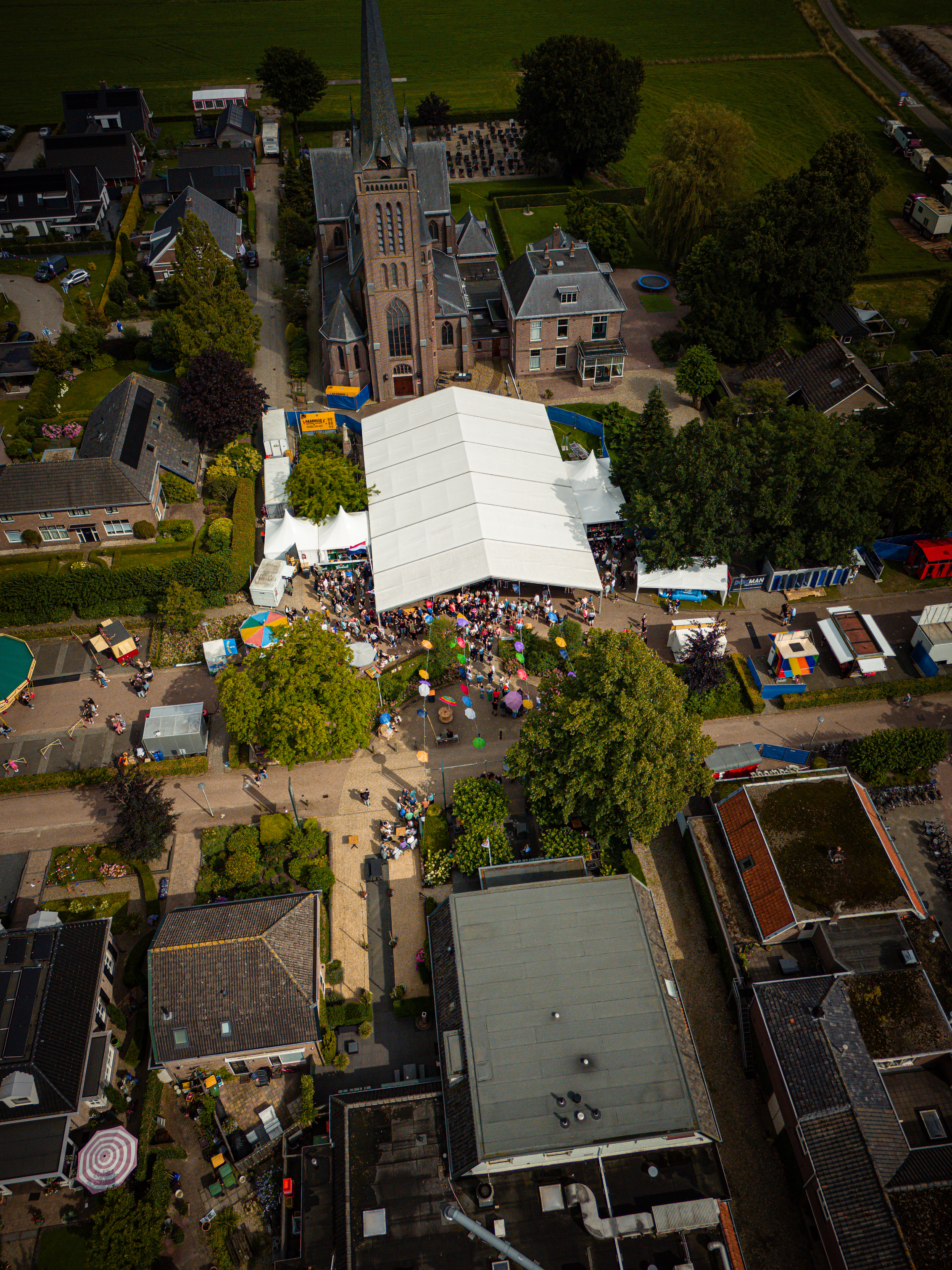 An aerial view of a church and park, where a large crowd has gathered for an outdoor market.