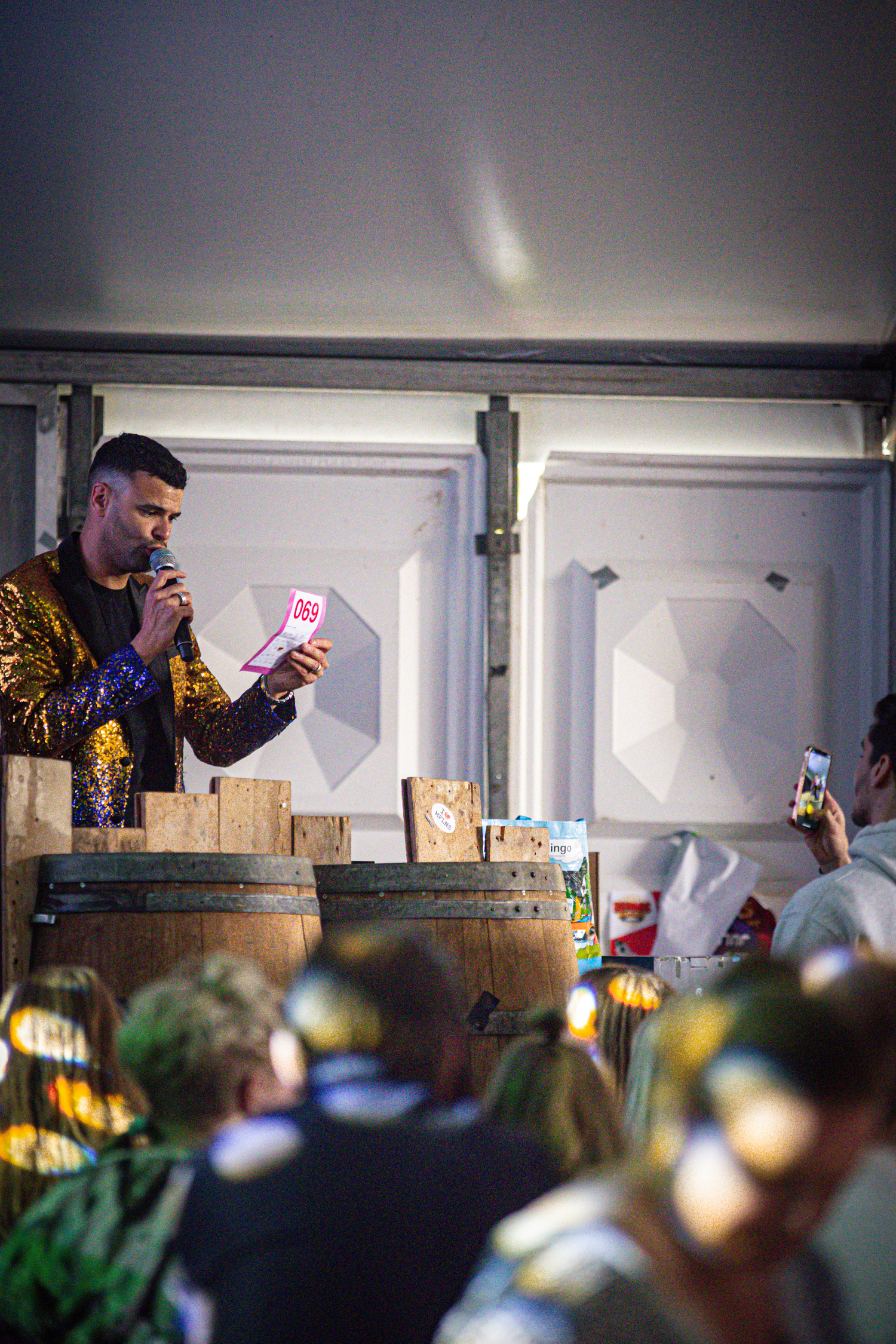 A man in a gold jacket on stage, holding a paper with pink and red writing.