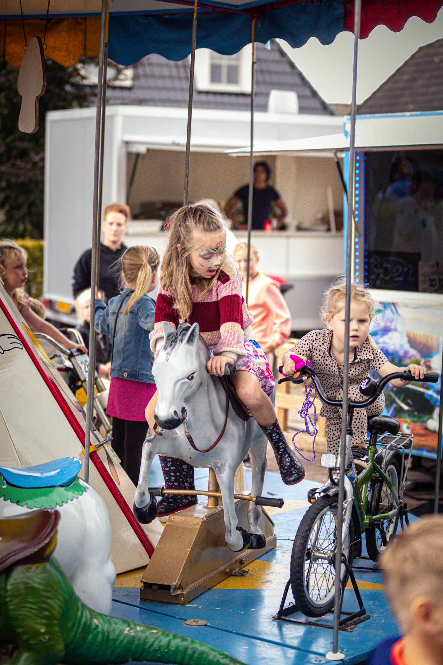 A few children are playing in a tent at the Kermis Boerhaar. They ride toy horses and bicycles.