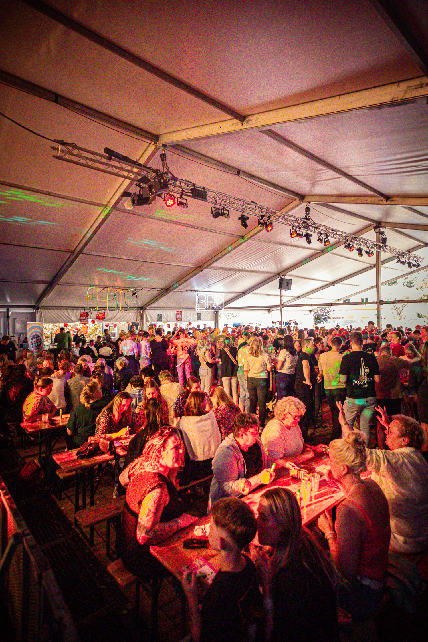 A group of people in a tented area, standing and sitting.