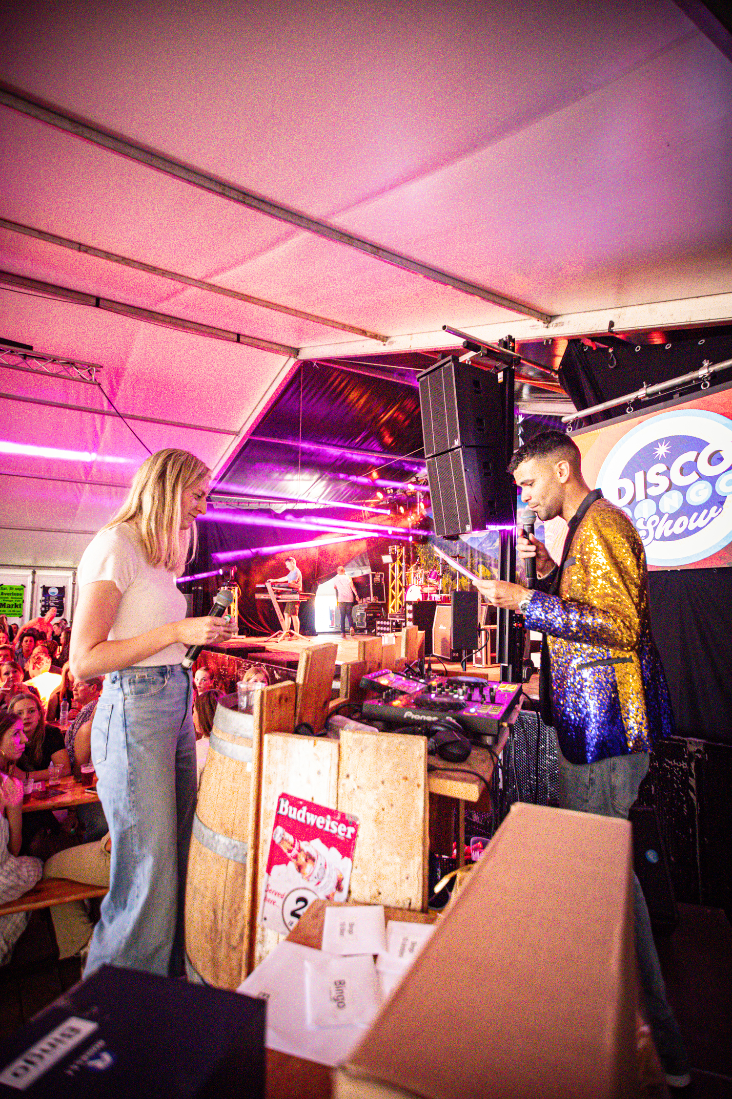 A man in a yellow jacket singing into a microphone on stage at the Kermis Boerhaar festival.