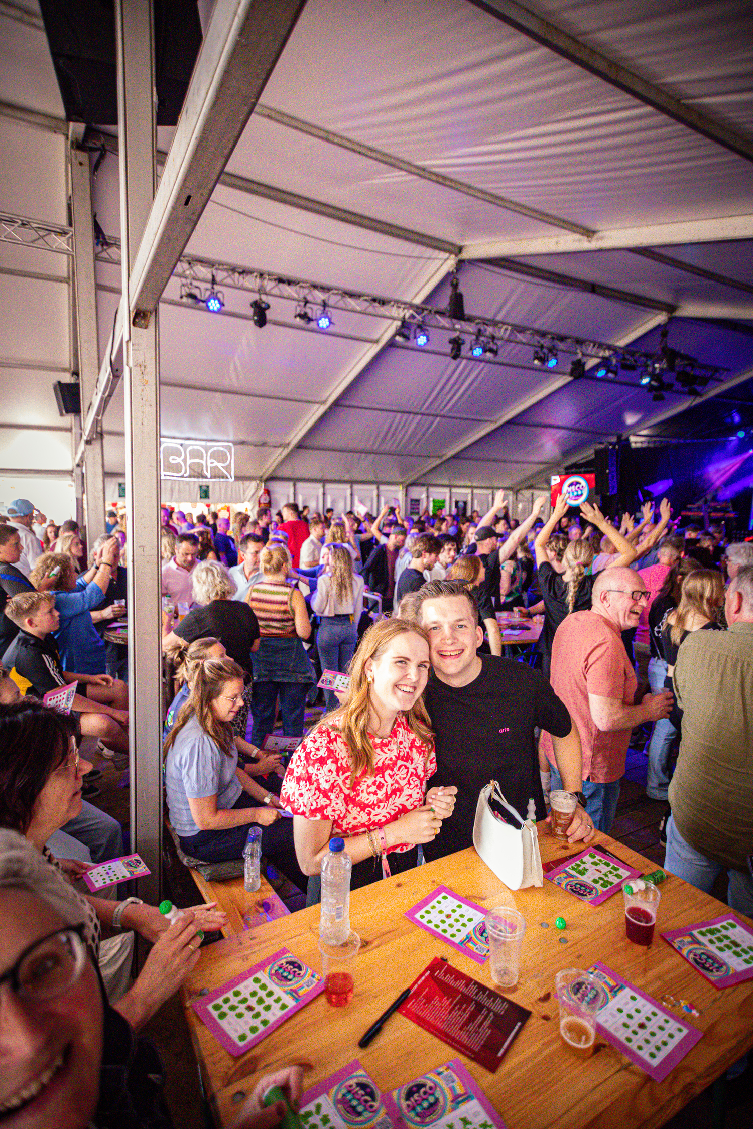 A group of people gather in a tent at the Kermis Boerhaar, enjoying the festivities with drinks and snacks.