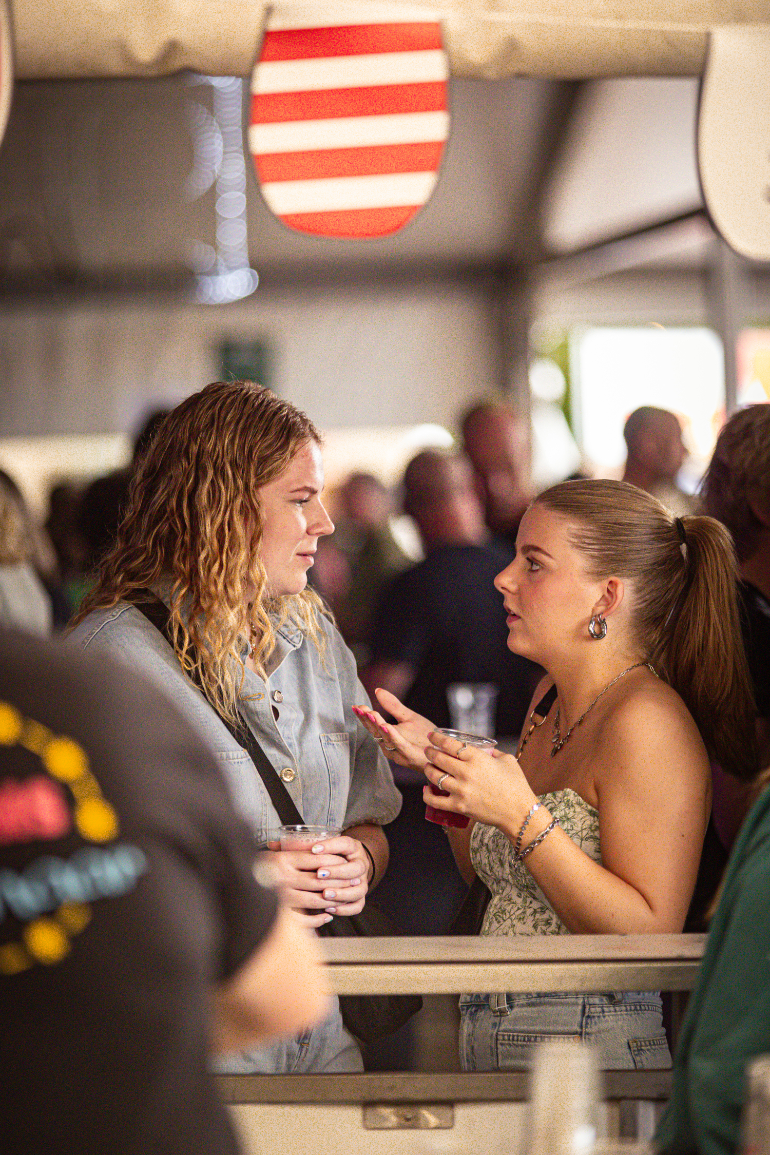 Two women talking at a bar with one wearing a heart shaped necklace.