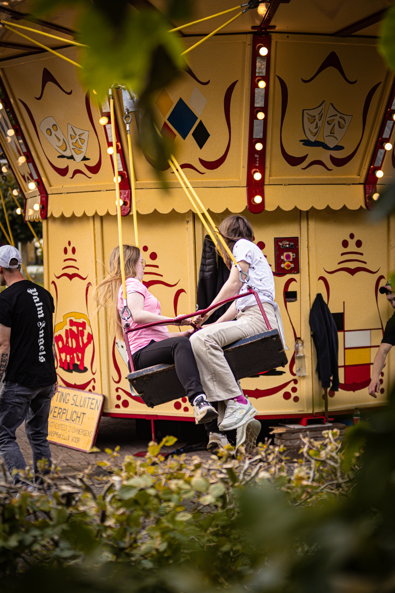 A woman and a boy are sitting on a swing at a carnival booth called "Middag & Avond".