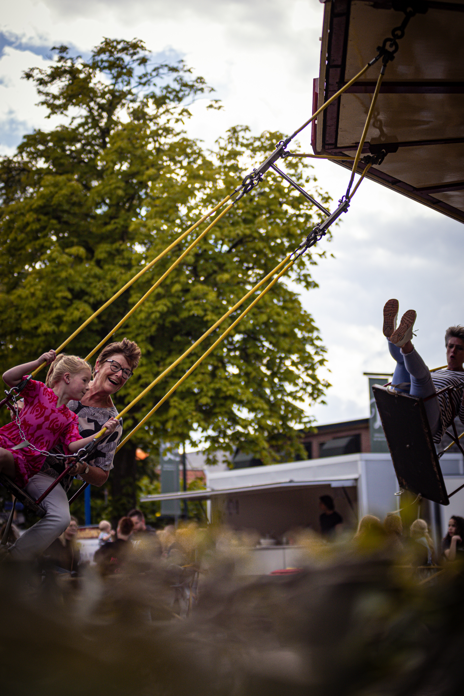 A family of 3 has a fun time swinging on a small swing in a park.