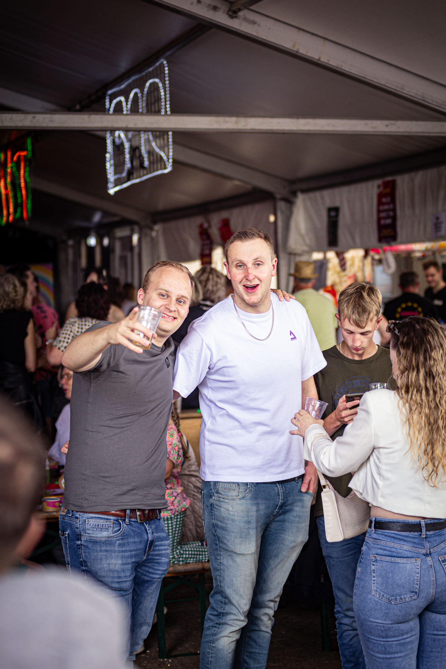 Three friends take a selfie together at an event, with the sign "Kermis Boerhaar" in the background.