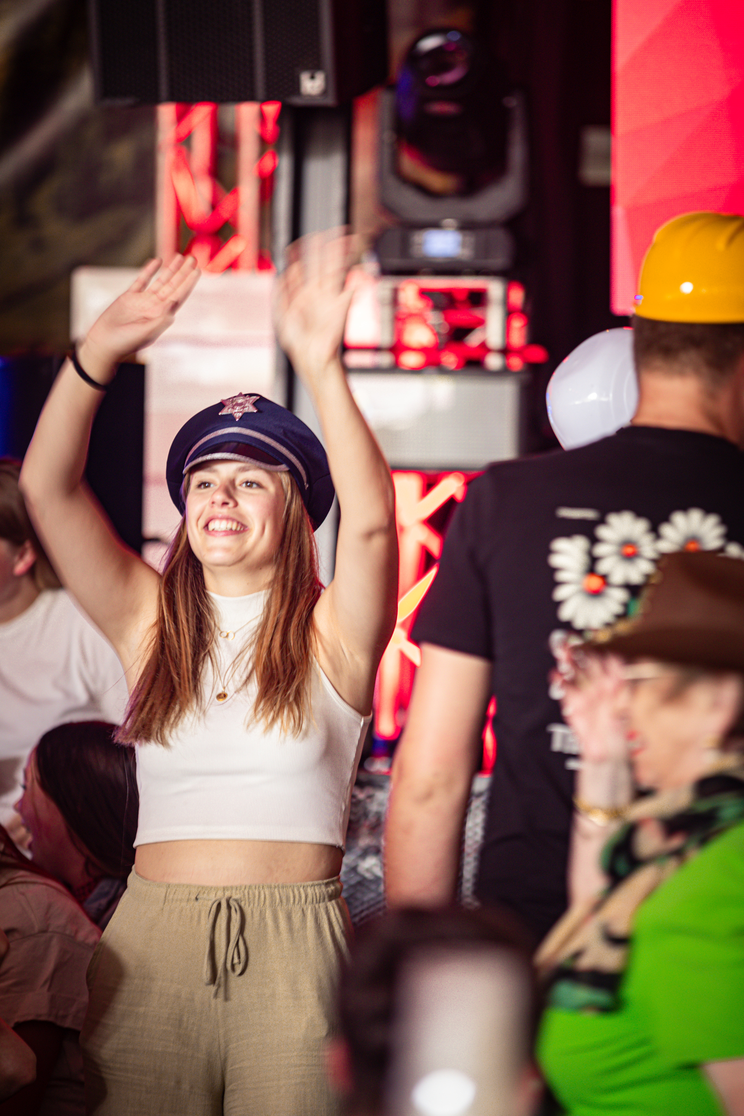 a woman wearing a blue hat and tan shorts in a crowd of people with her arms up.