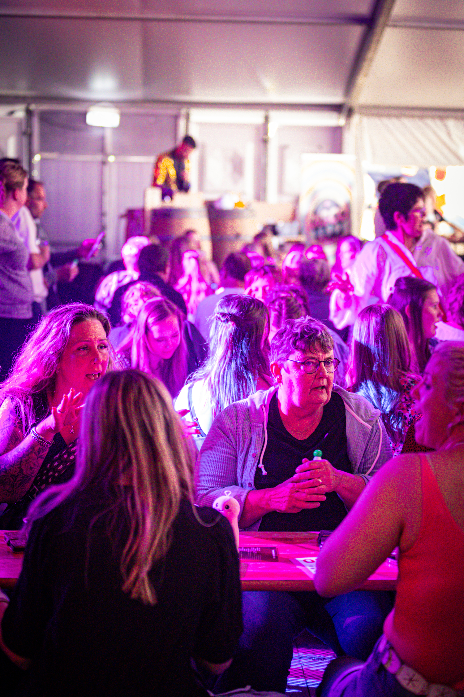 People are gathered in a large tent with purple lights, enjoying themselves at an event.