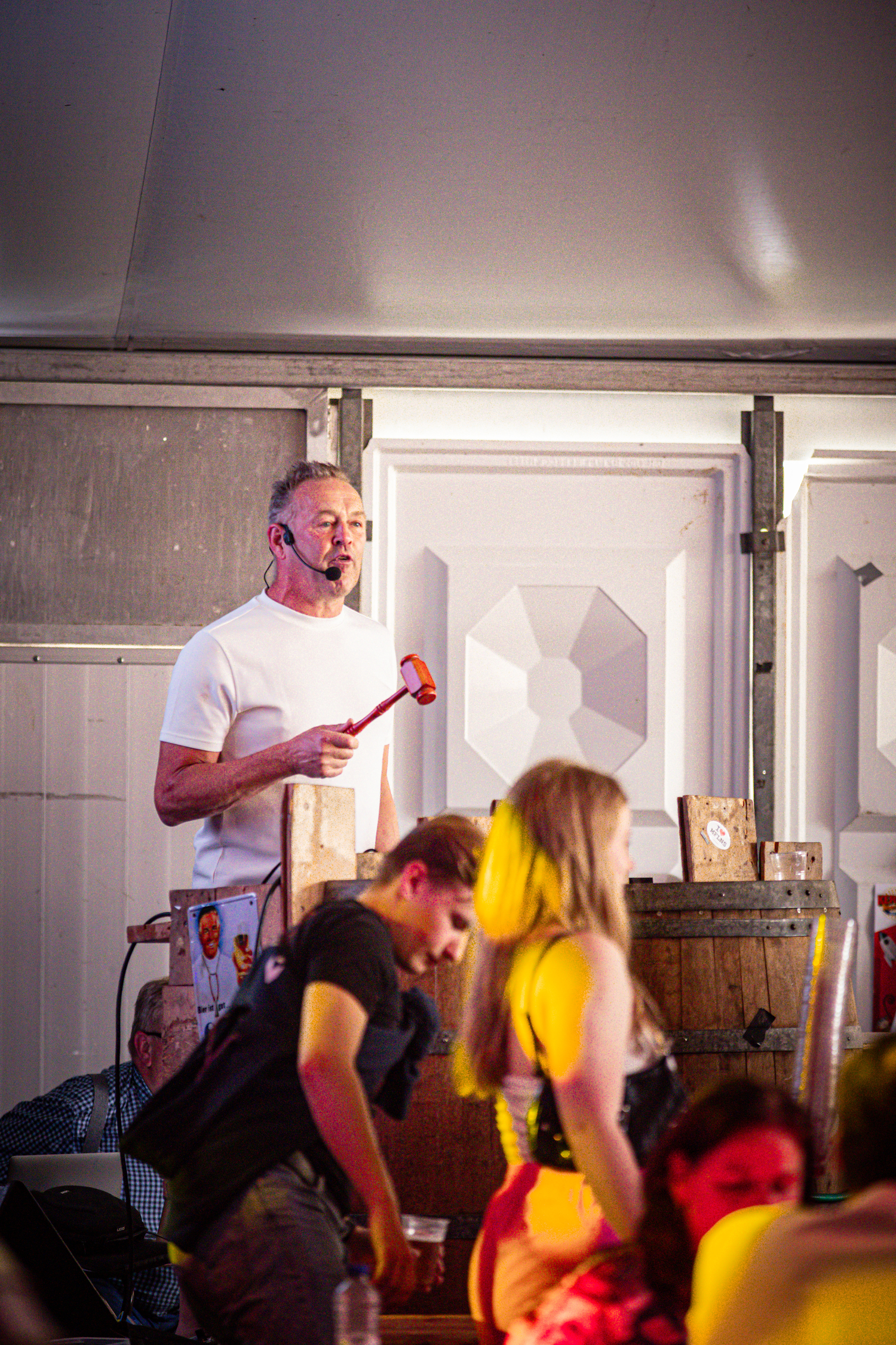 A man stands behind a table holding a red and black microphone while people look at him.