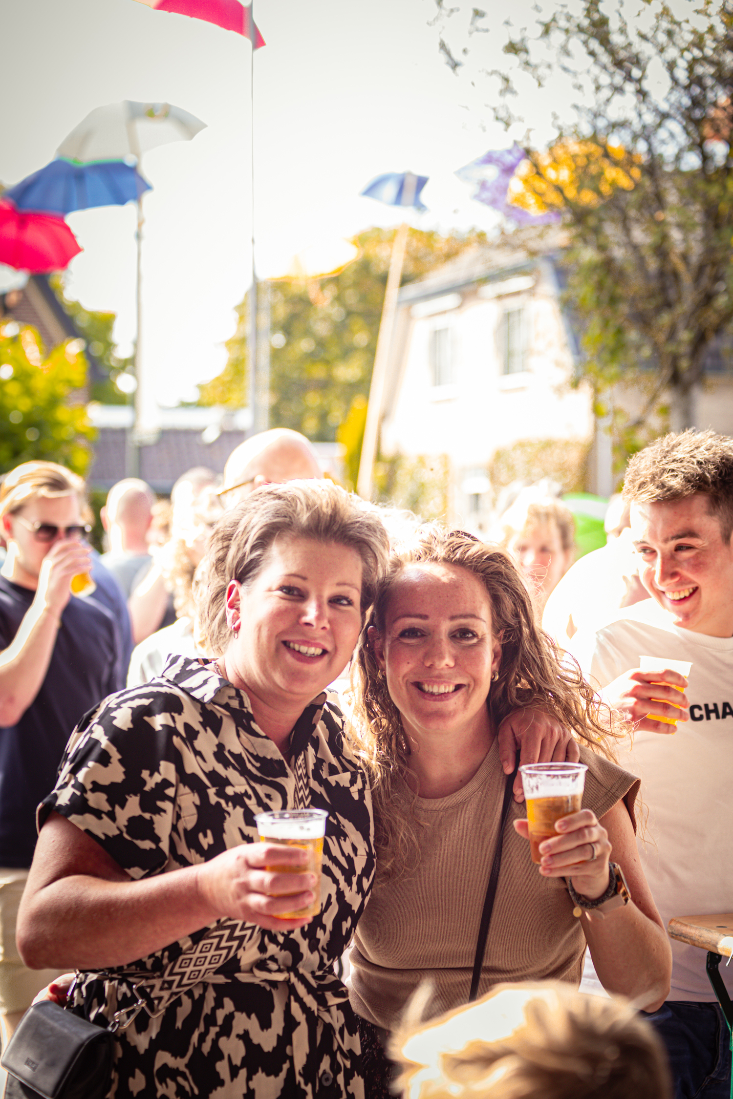 A photo of two women smiling together at an outdoor event, one holding a beer in her right hand.