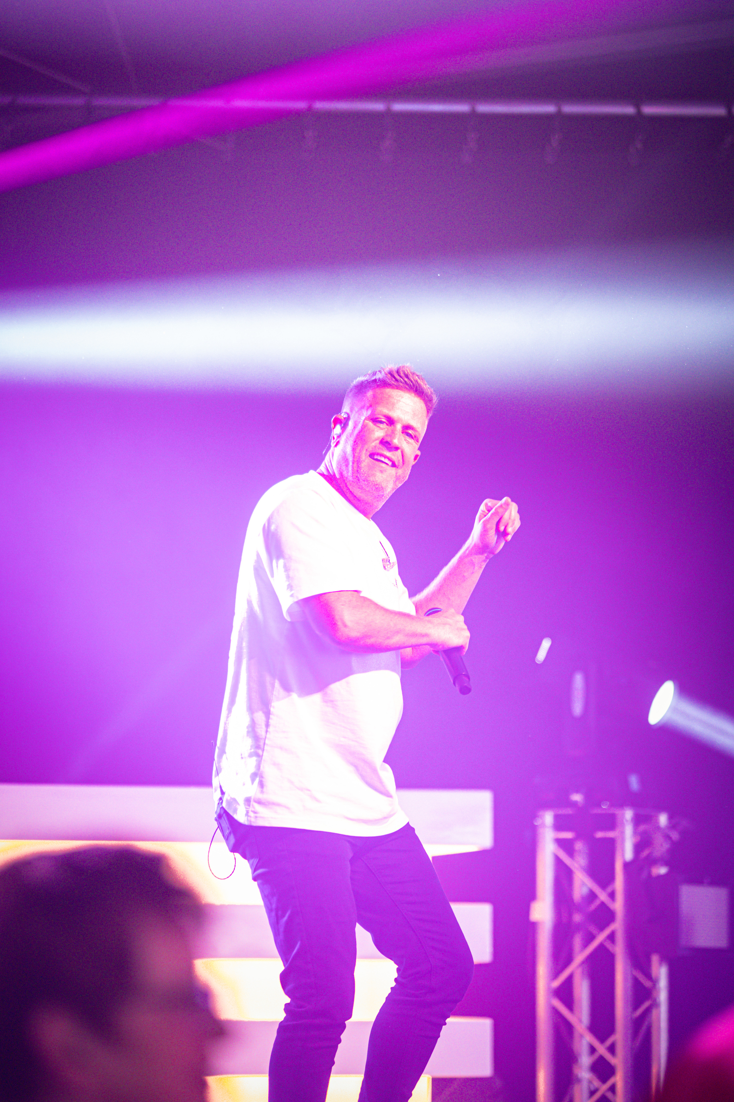 A man is on stage with a microphone, wearing a white shirt.