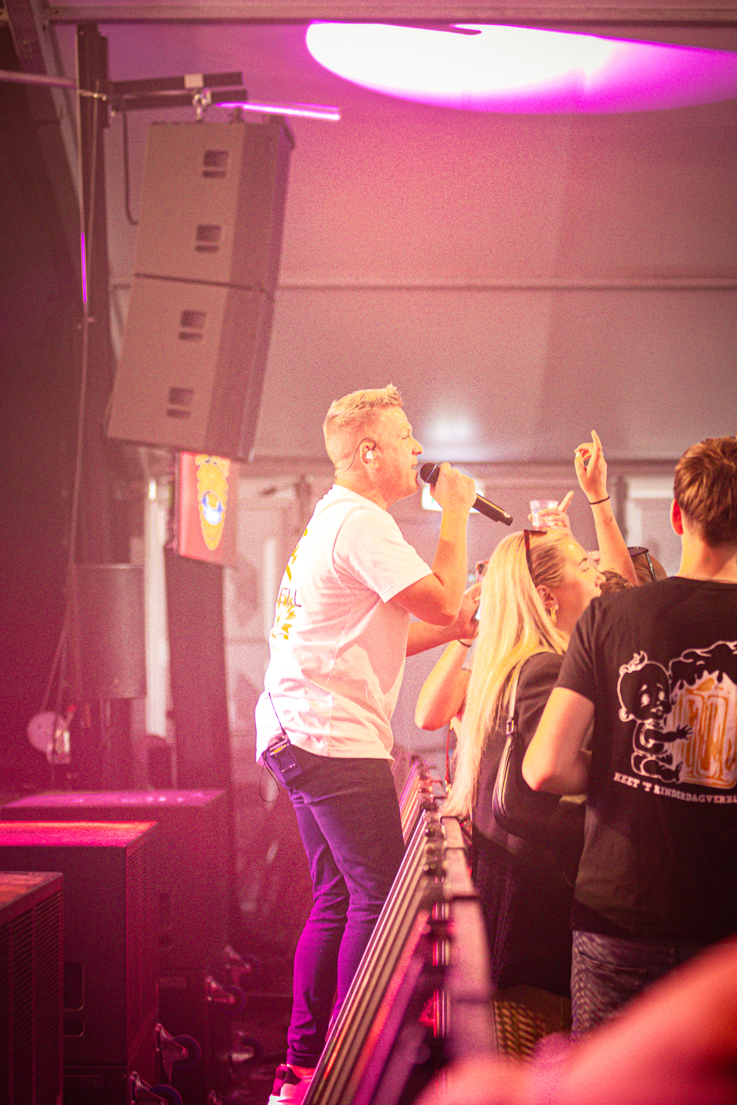 A man in a white shirt singing into the microphone while two girls are taking pictures.