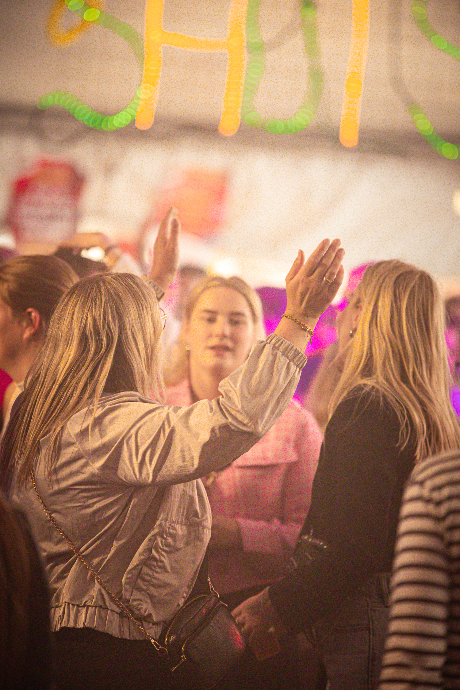 Several women are standing in a circle at a festival, waving to each other and smiling.