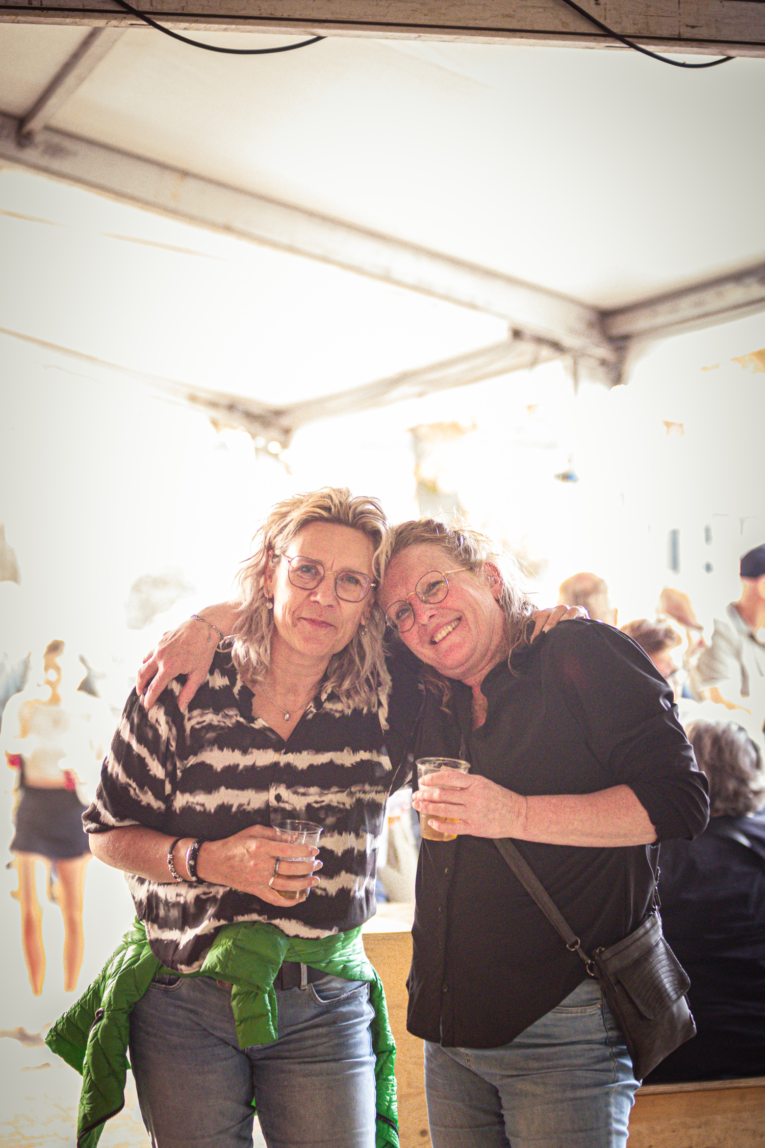 Two women in a tent with one wearing a striped shirt and the other wearing a black top holding hands.